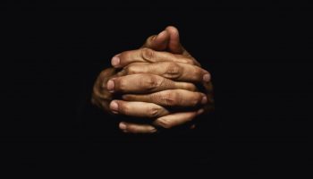 Male hands crossed for prayer in dark